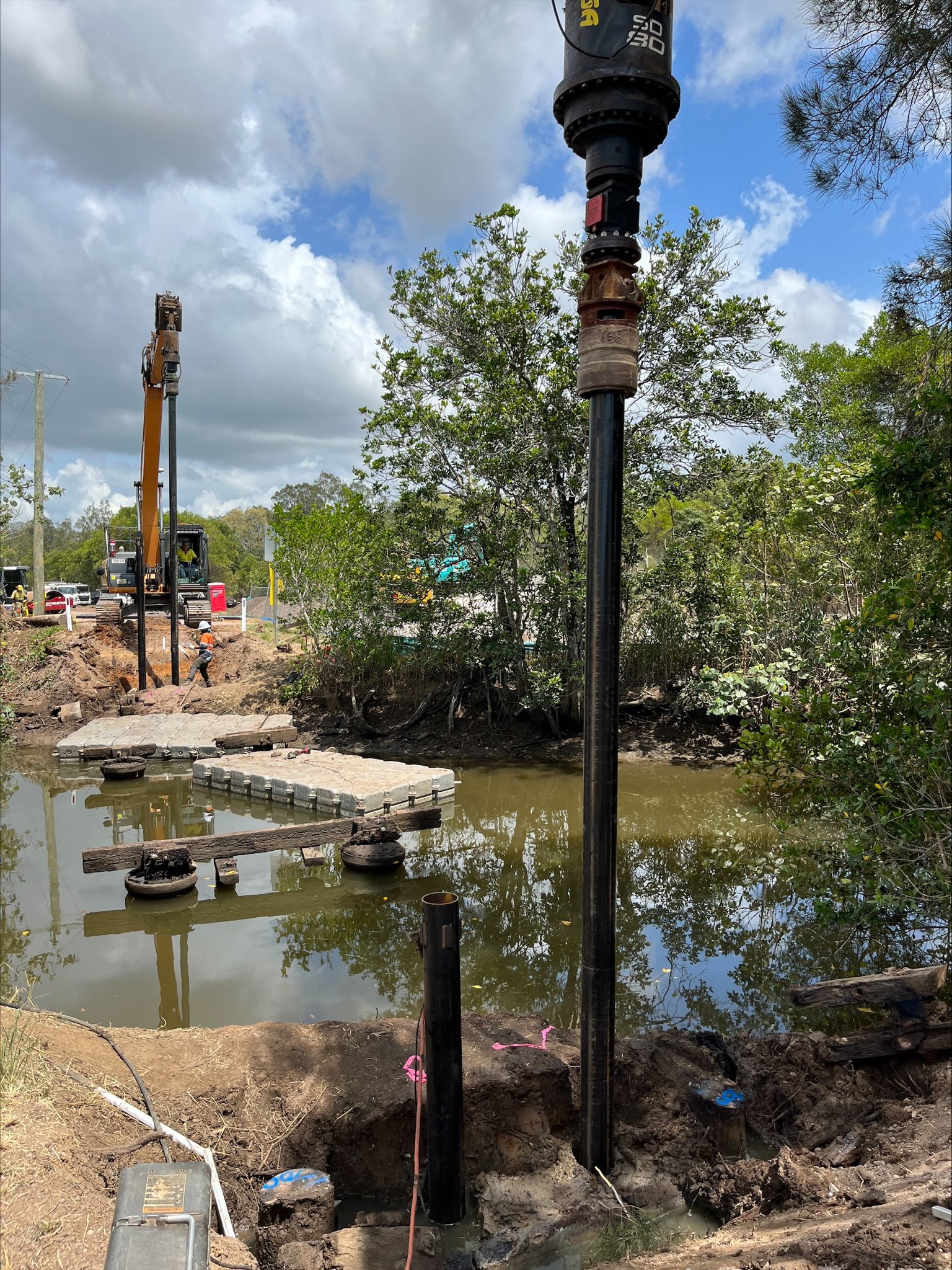 Timber restoration Services crew screw piling along bank before beginning of installing new bridge.